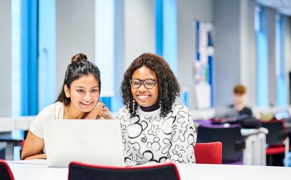 Two Newcastle University Business School students looking at their laptop and smiling